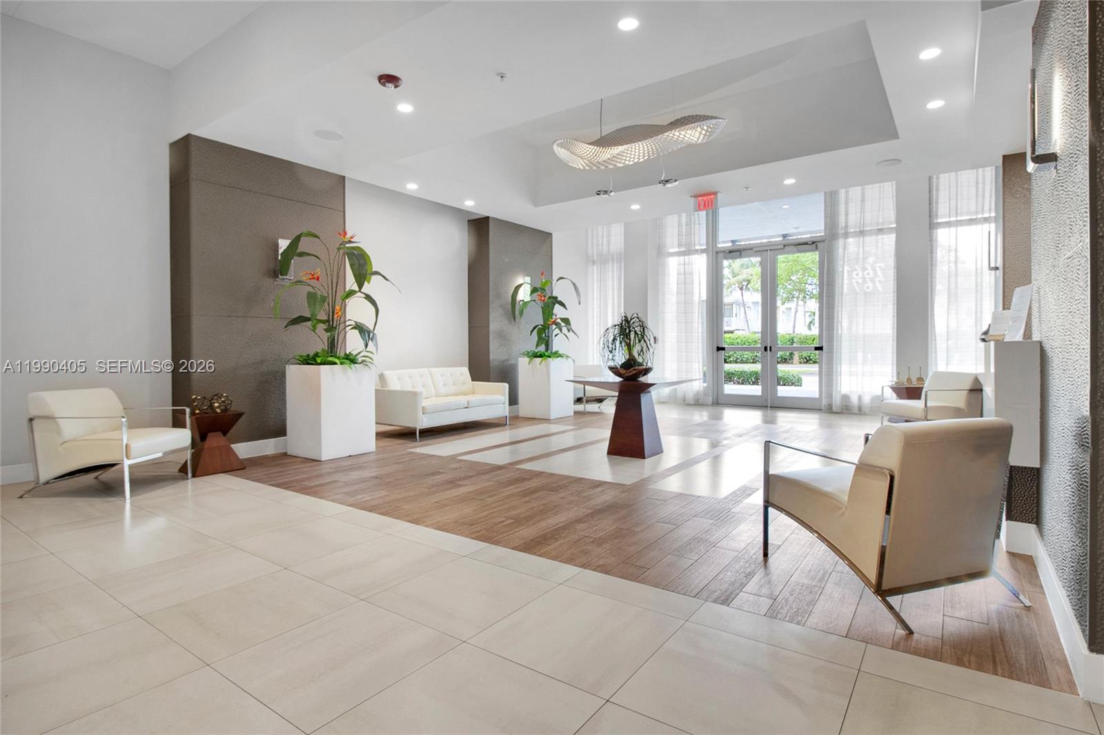 A modern building lobby features white leather chairs, a central table, and large potted plants — 7661 NW 107th Ave # 501, Doral FL 33178, DORAL, FL