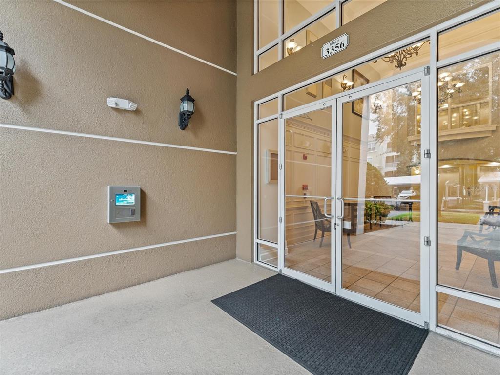 The exterior entrance of a building features glass double doors, wall-mounted lights, and a keypad — 3356 ROBERT TRENT JONES DRIVE UNIT 407, ORLANDO, FL