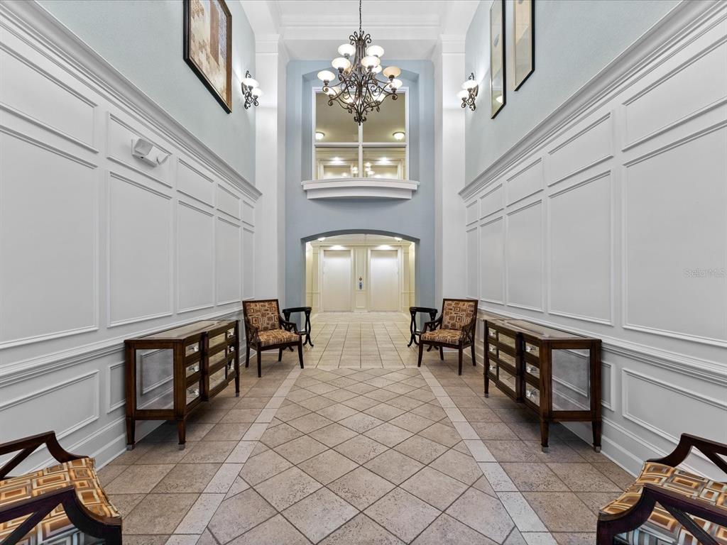 A symmetrical lobby features white wainscoting, a chandelier, two mirrored consoles, and two elevators — 3356 ROBERT TRENT JONES DRIVE UNIT 407, ORLANDO, FL
