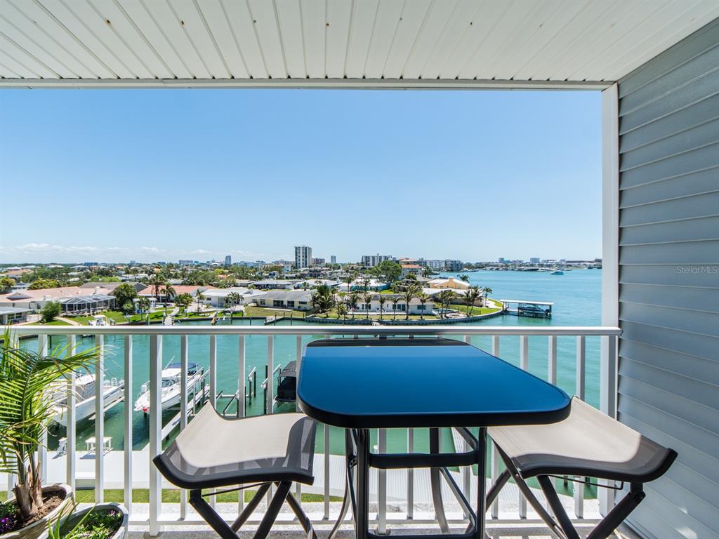 A balcony with a small table and two chairs overlooks a canal and city skyline — 610 ISLAND WAY UNIT 407, CLEARWATER BEACH, FL