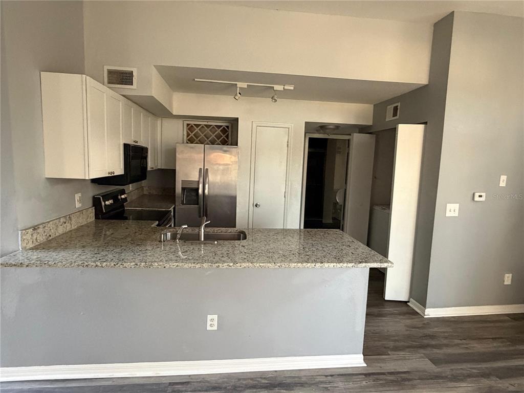 A kitchen features white cabinets, granite countertops, stainless steel appliances, and a breakfast bar — 7250 WESTPOINTE BOULEVARD UNIT 1034, ORLANDO, FL