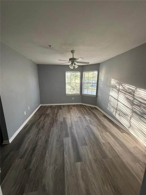 An empty room features gray walls, wood-look flooring, a ceiling fan, and two windows — 7250 WESTPOINTE BOULEVARD UNIT 1034, ORLANDO, FL