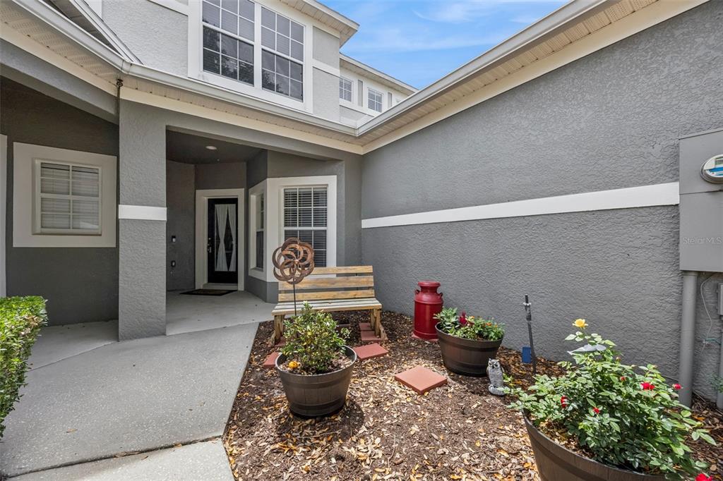 A gray house exterior features a covered entryway, a wooden bench, and potted plants — 1422 TRAVERTINE TERRACE, SANFORD, FL