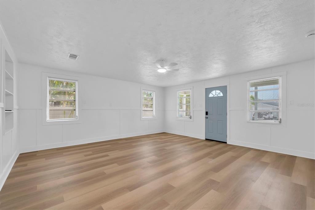 An empty room with white walls, light wood-look flooring, a ceiling fan, and a blue door — 358 BOCA CIEGA DRIVE, MADEIRA BEACH, FL