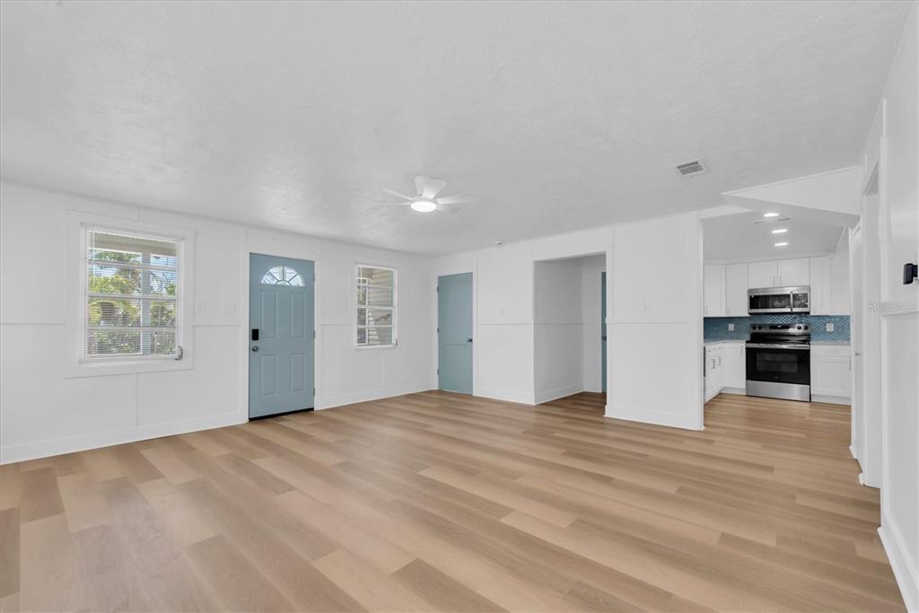 A bright living room with light wood flooring, white walls, and a blue front door — 358 BOCA CIEGA DRIVE, MADEIRA BEACH, FL