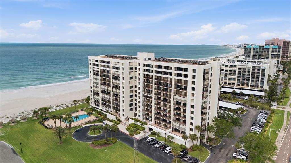 An aerial view shows a large beachfront apartment building with a pool and parking lot — 1460 GULF BOULEVARD UNIT 501, CLEARWATER, FL