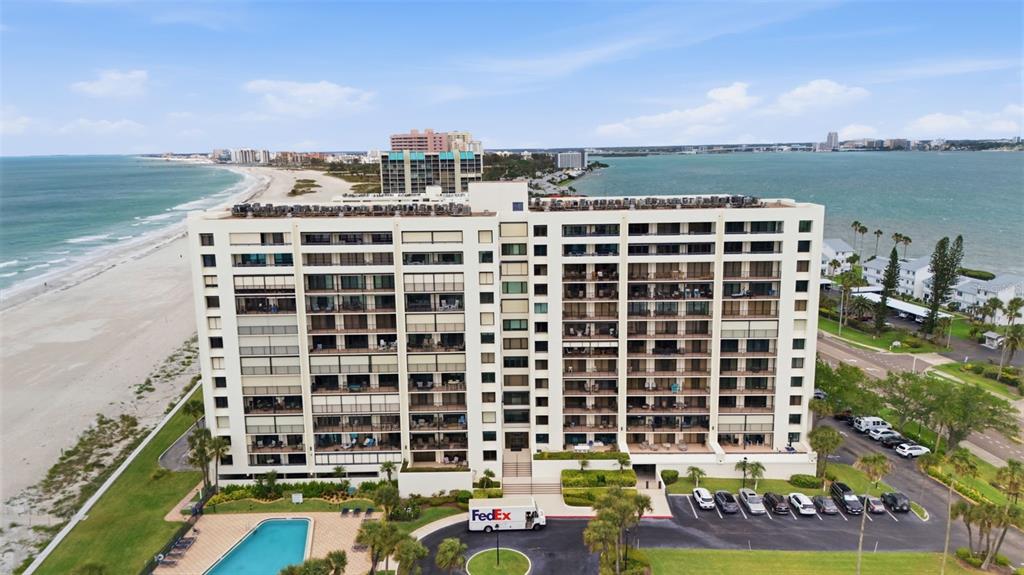 An aerial view shows a large beachfront apartment building with a pool and parking lot — 1460 GULF BOULEVARD UNIT 501, CLEARWATER, FL