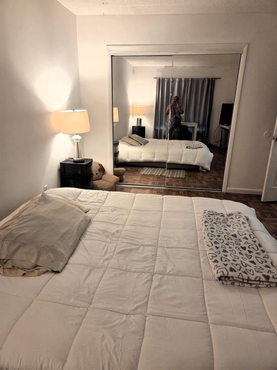 A bedroom features a white comforter, a bedside lamp, and mirrored sliding closet doors — 5965 Caribbean Boulevard, West Palm Beach FL 33407, WEST PALM BEACH, FL