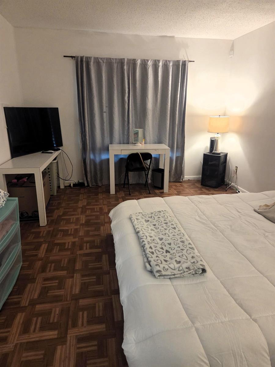 A bedroom with parquet flooring, a bed, a desk, a vanity, and grey curtains — 5965 Caribbean Boulevard, West Palm Beach FL 33407, WEST PALM BEACH, FL
