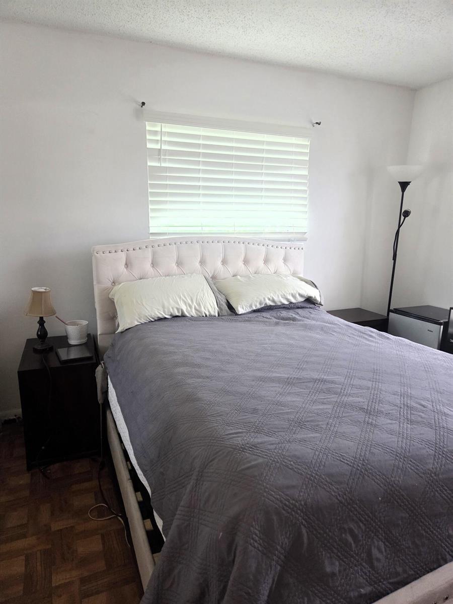 A bedroom features a tufted headboard, a gray quilt, and a window with white blinds — 5965 Caribbean Boulevard, West Palm Beach FL 33407, WEST PALM BEACH, FL