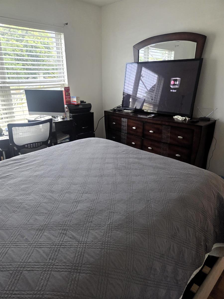 A bedroom features a bed with a gray quilt, a dresser with a television, and a desk — 5965 Caribbean Boulevard, West Palm Beach FL 33407, WEST PALM BEACH, FL