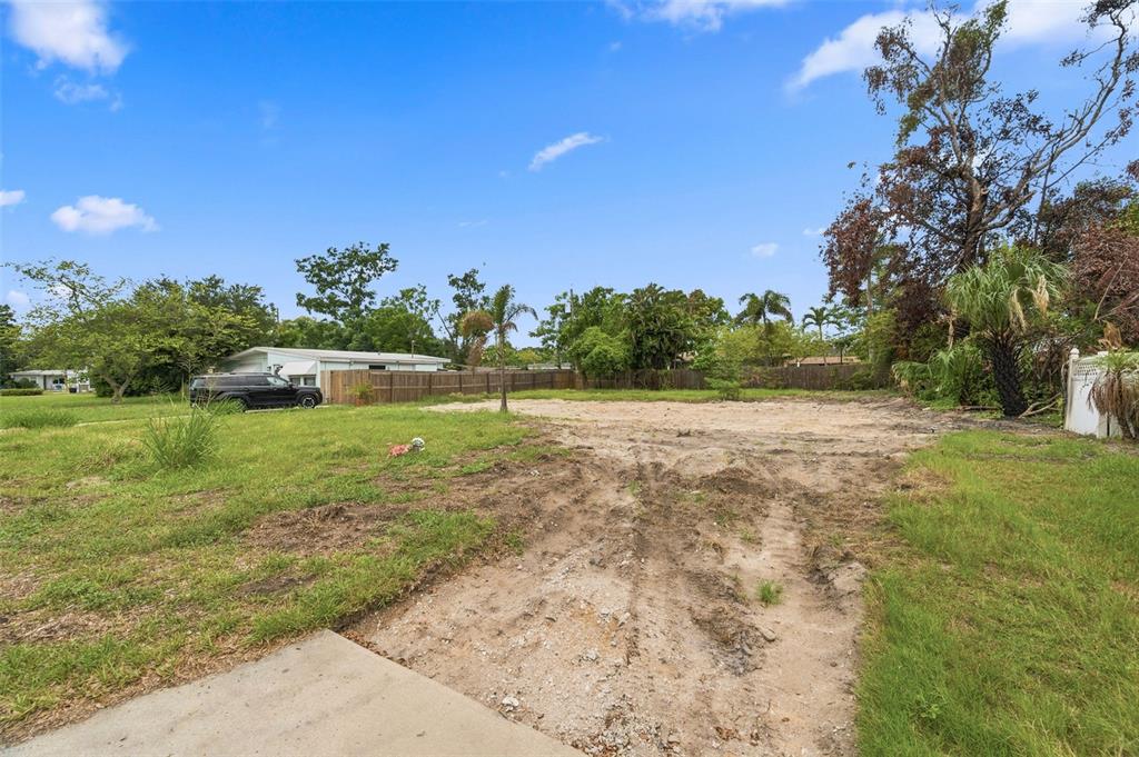 A vacant, grassy residential lot with tire tracks leading toward a wooden fence and trees — 3963 NEPTUNE DRIVE SE, ST PETERSBURG, FL