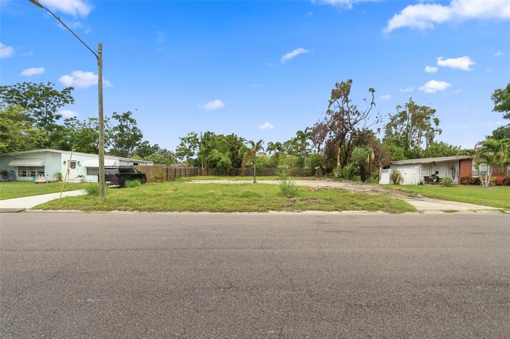 A vacant, grassy residential lot sits between two single-story houses under a blue sky — 3963 NEPTUNE DRIVE SE, ST PETERSBURG, FL