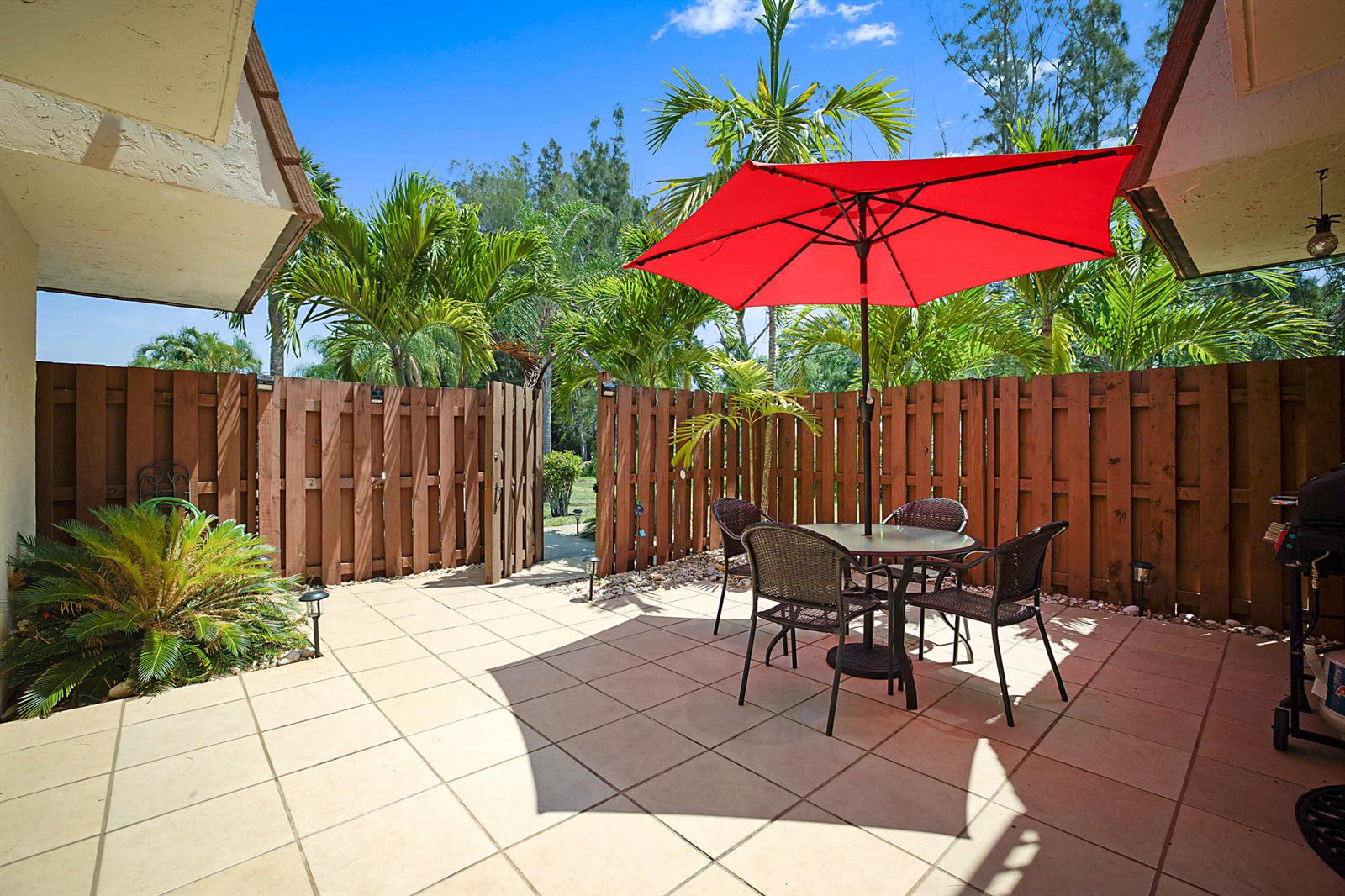 A tiled patio features a dining set under a red umbrella, enclosed by wooden fencing — 825 Center Street # 11c, Jupiter FL 33458, JUPITER, FL