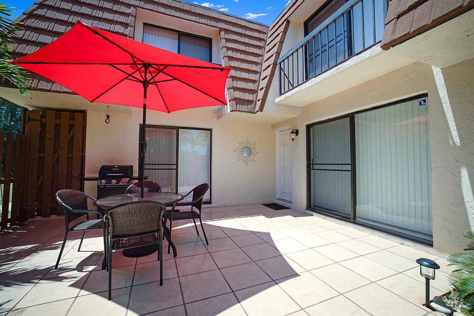 A paved patio features a dining set with a red umbrella and a barbecue grill — 825 Center Street # 11c, Jupiter FL 33458, JUPITER, FL