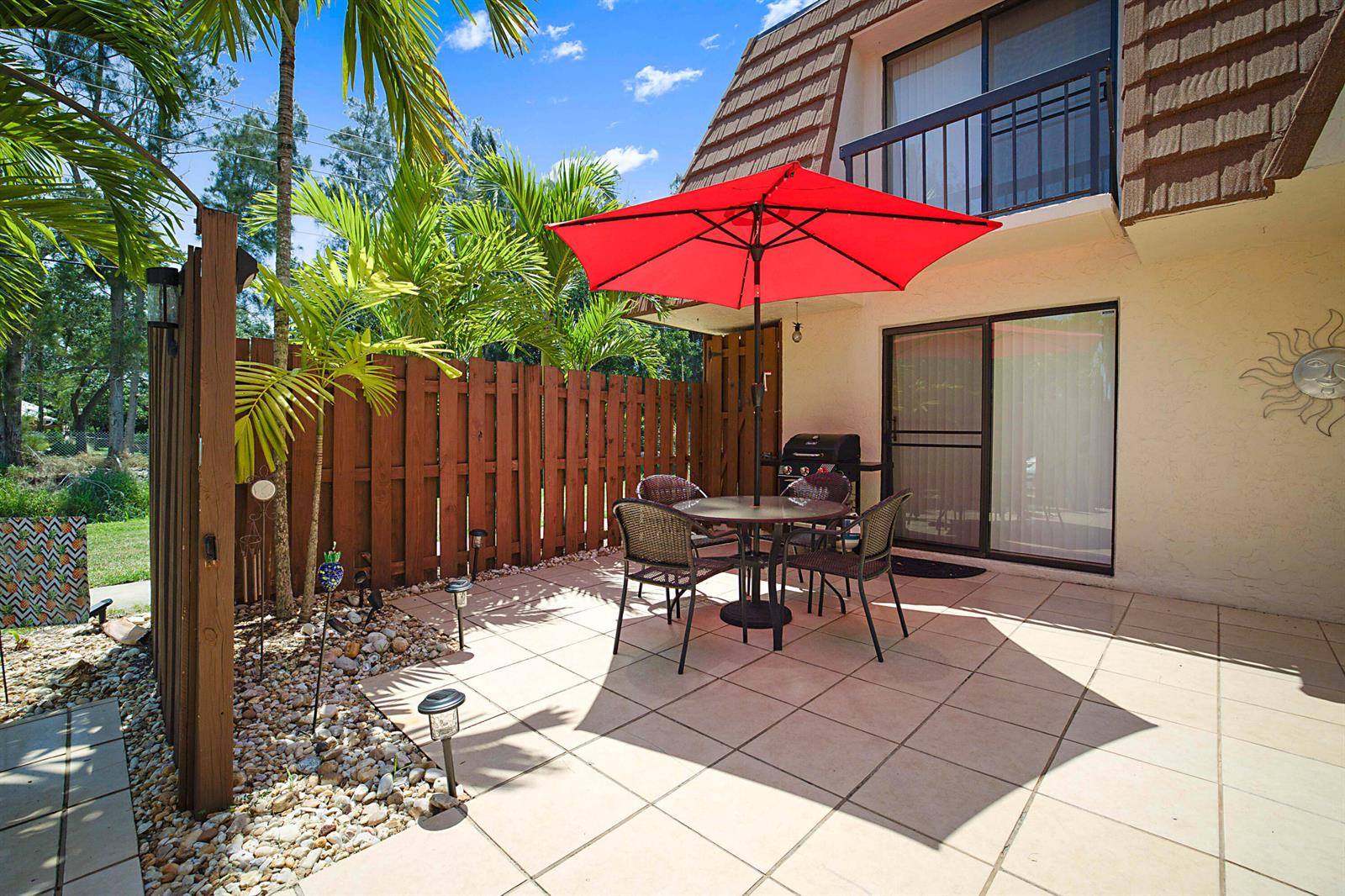 A patio with a red umbrella, outdoor dining set, and wooden fence next to a building — 825 Center Street # 11c, Jupiter FL 33458, JUPITER, FL