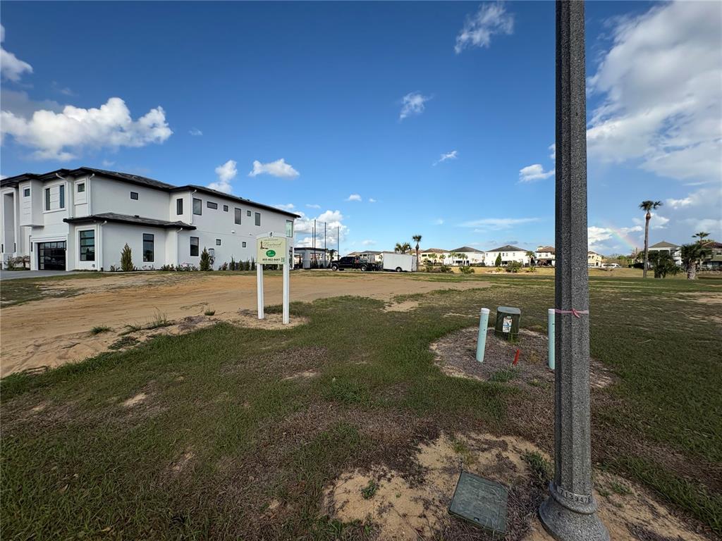 A vacant lot with a sign stands next to a modern two-story house — 1153 GRAND TRAVERSE PARKWAY, REUNION, FL