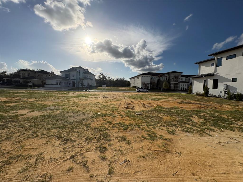 A vacant, sandy residential lot sits between several large, modern multi-story houses — 1153 GRAND TRAVERSE PARKWAY, REUNION, FL