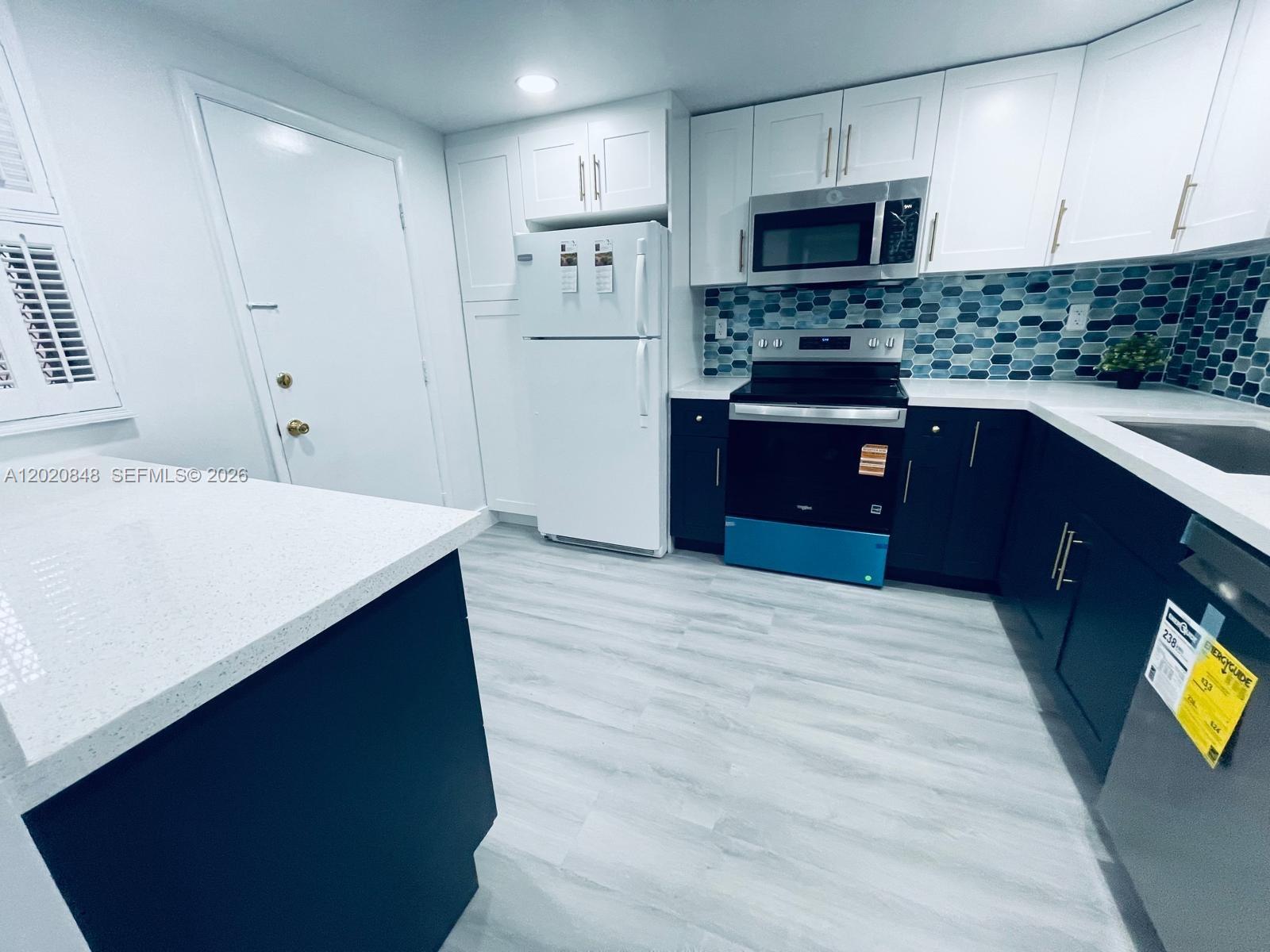 A kitchen features white upper cabinets, dark lower cabinets, a blue tiled backsplash, and appliances — 9175 SW 77th Ave # 306, Miami FL 33156, MIAMI, FL