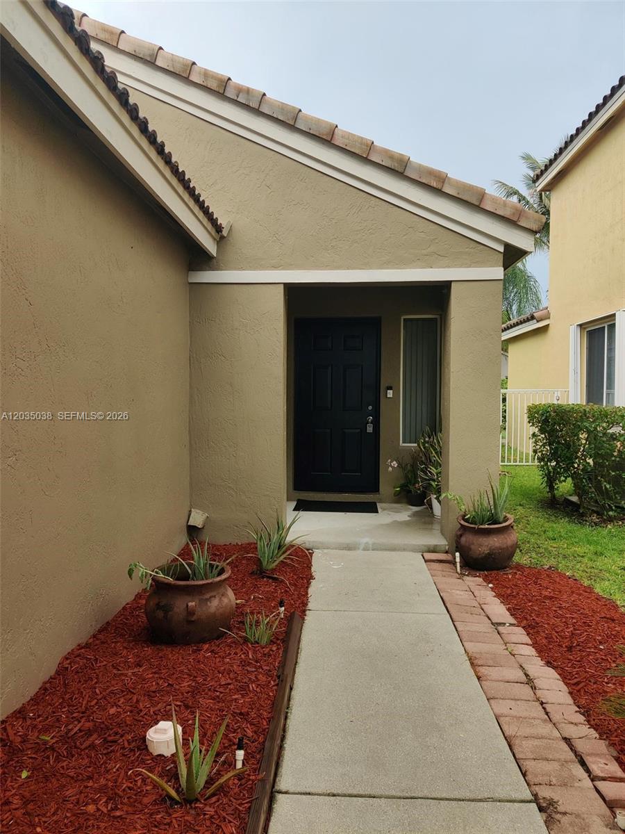 A concrete walkway leads to the black front door of a tan stucco house — 4315 Greenbriar Ln, Weston FL 33331, WESTON, FL
