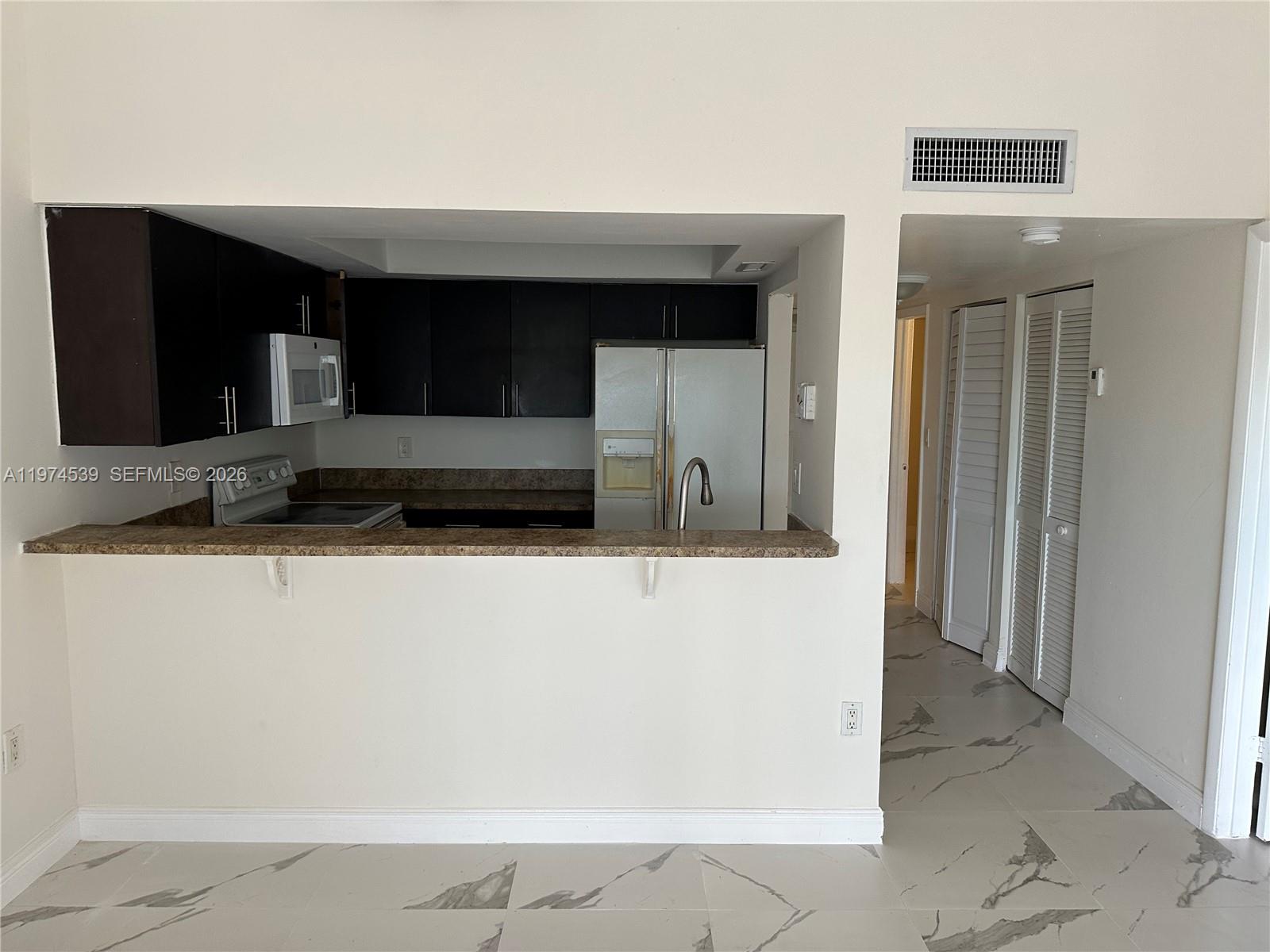 A kitchen with dark cabinets and a breakfast bar overlooks a tiled hallway — 16220 NW 2nd Ave # 512, Miami FL 33169, MIAMI, FL