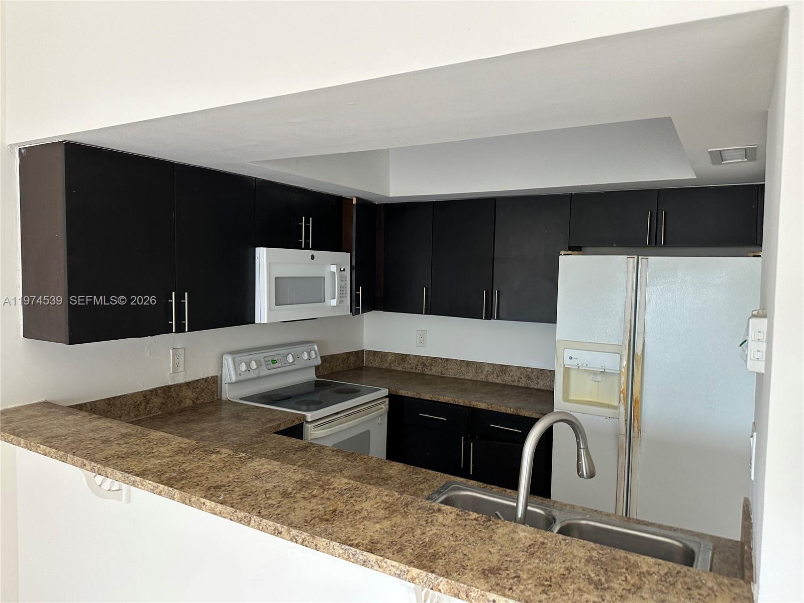 A kitchen features dark cabinets, white appliances, and brown laminate countertops with a breakfast bar — 16220 NW 2nd Ave # 512, Miami FL 33169, MIAMI, FL