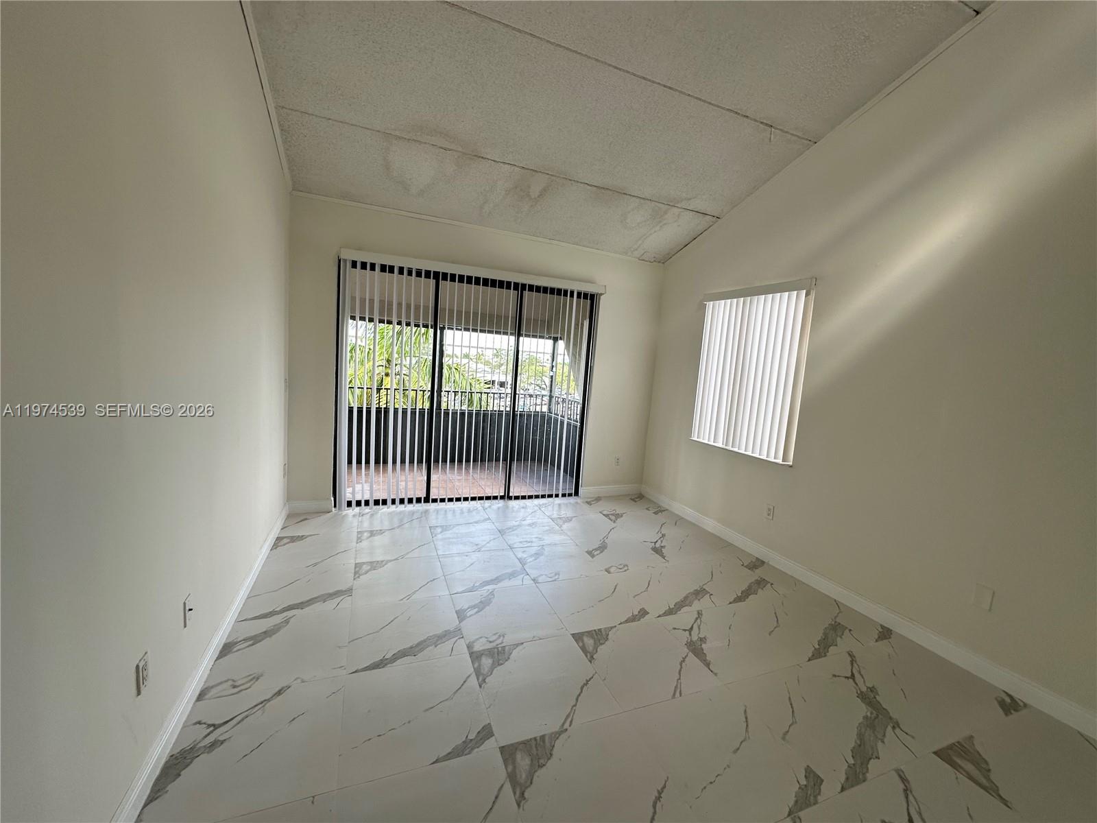 An empty room features white marble-patterned tile floors, a vaulted ceiling, and a sliding glass door — 16220 NW 2nd Ave # 512, Miami FL 33169, MIAMI, FL