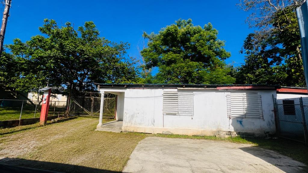 A single-story white house with louvered windows sits on a lot with a concrete driveway — CO Villa Caridad AMPARO ST. UNIT D-10, CAROLINA, PR