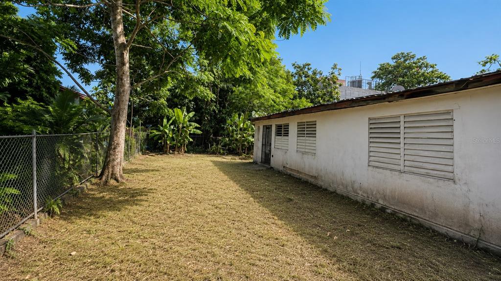 A side yard features a chain-link fence, a large tree, and a white exterior wall — CO Villa Caridad AMPARO ST. UNIT D-10, CAROLINA, PR