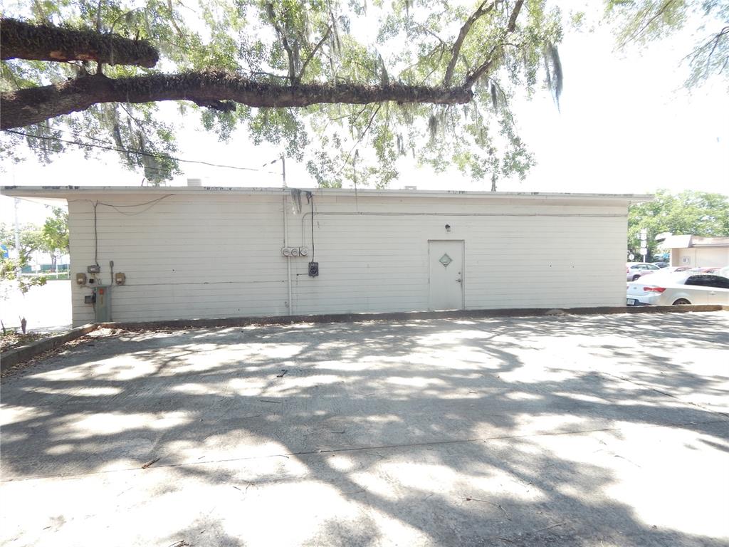 A white, single-story building exterior with a door and parking lot under a large tree — 1503 N MAIN STREET, KISSIMMEE, FL