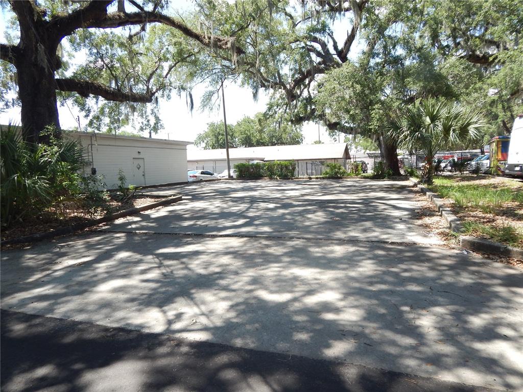 A paved parking lot sits in front of a white building under large oak trees — 1503 N MAIN STREET, KISSIMMEE, FL