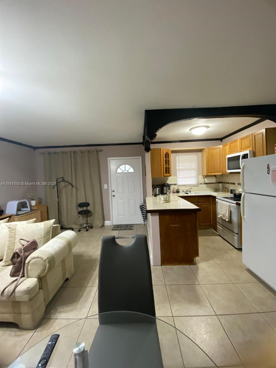 An open-concept kitchen with wood cabinets and a breakfast bar overlooks a living area — 4050 NW 135th St # 1, Opa-Locka FL 33054, OPA-LOCKA, FL