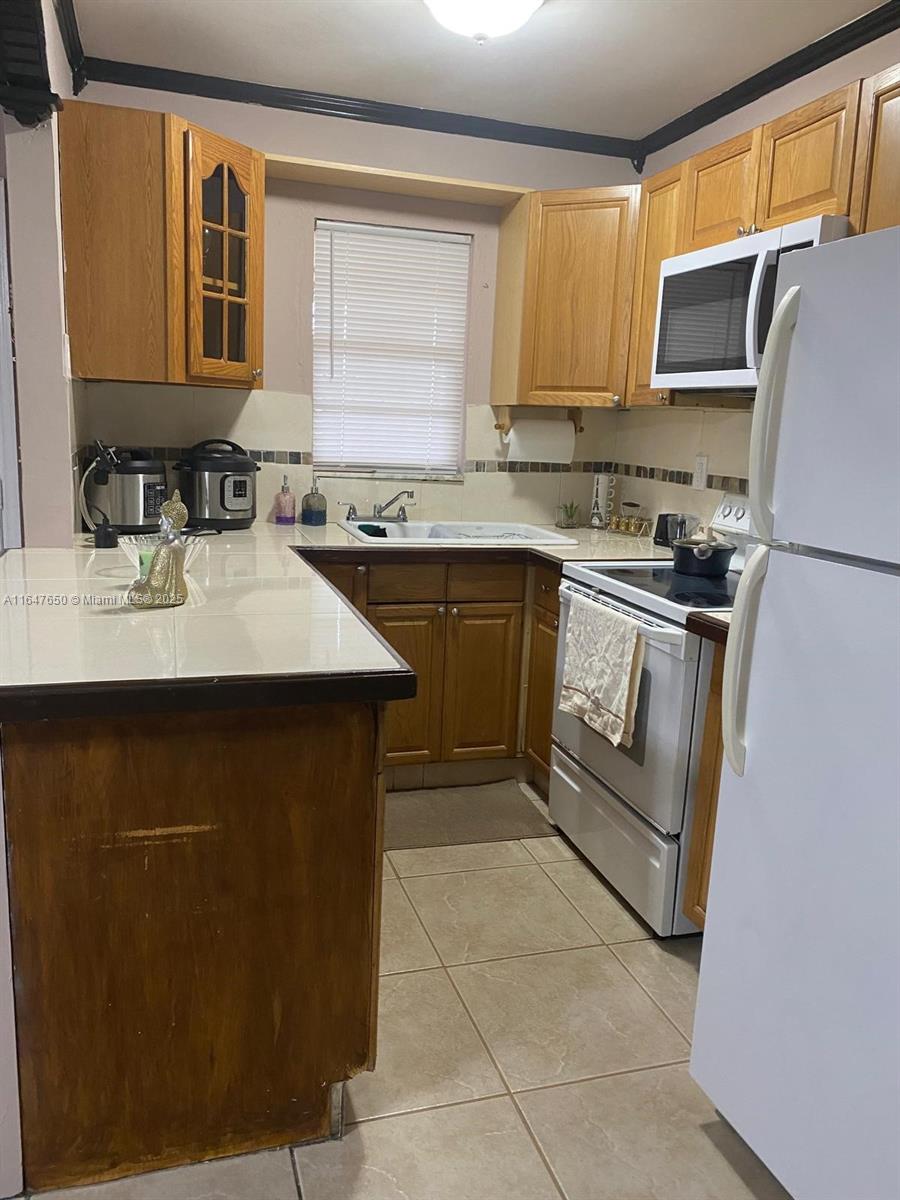 A kitchen features wood cabinets, white tile countertops, a white appliance suite, and tiled flooring — 4050 NW 135th St # 1, Opa-Locka FL 33054, OPA-LOCKA, FL
