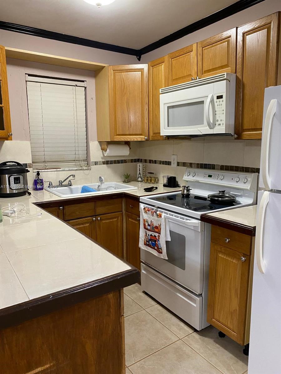 A kitchen features wood cabinets, tile countertops, a white stove, and a window above the sink — 4050 NW 135th St # 1, Opa-Locka FL 33054, OPA-LOCKA, FL