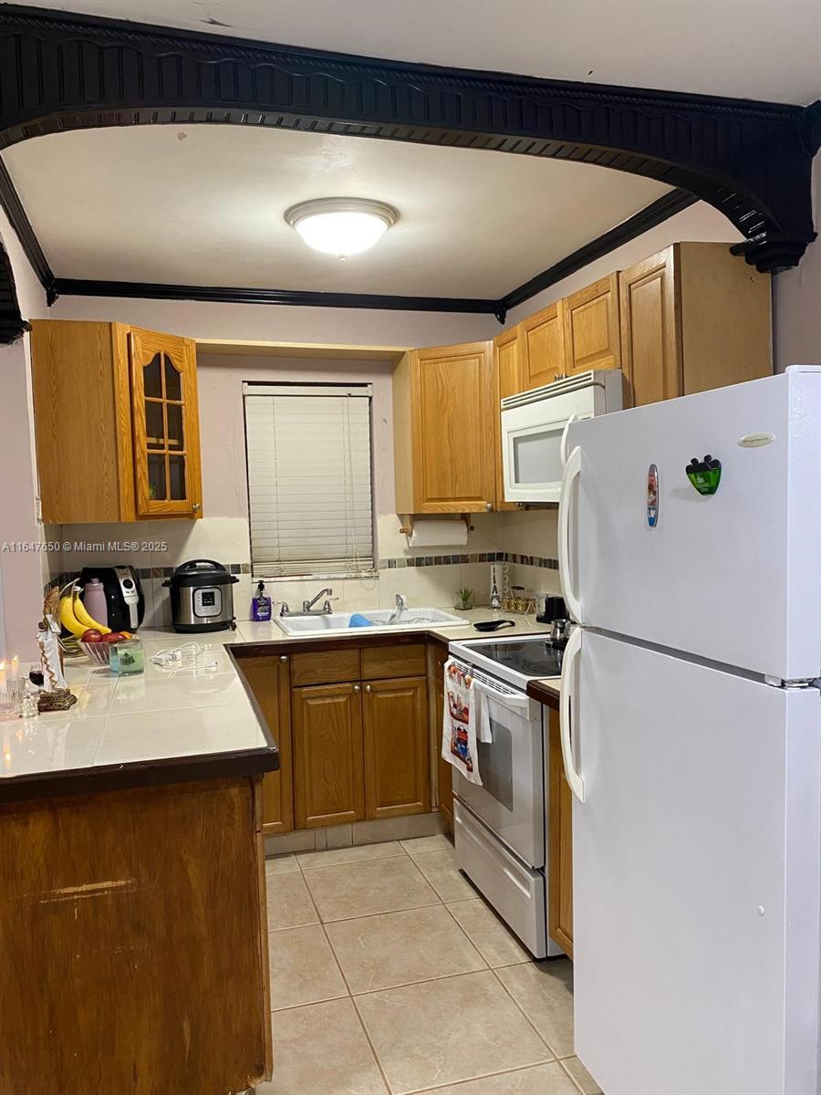 A kitchen features light wood cabinets, white tile countertops, and a white refrigerator — 4050 NW 135th St # 1, Opa-Locka FL 33054, OPA-LOCKA, FL