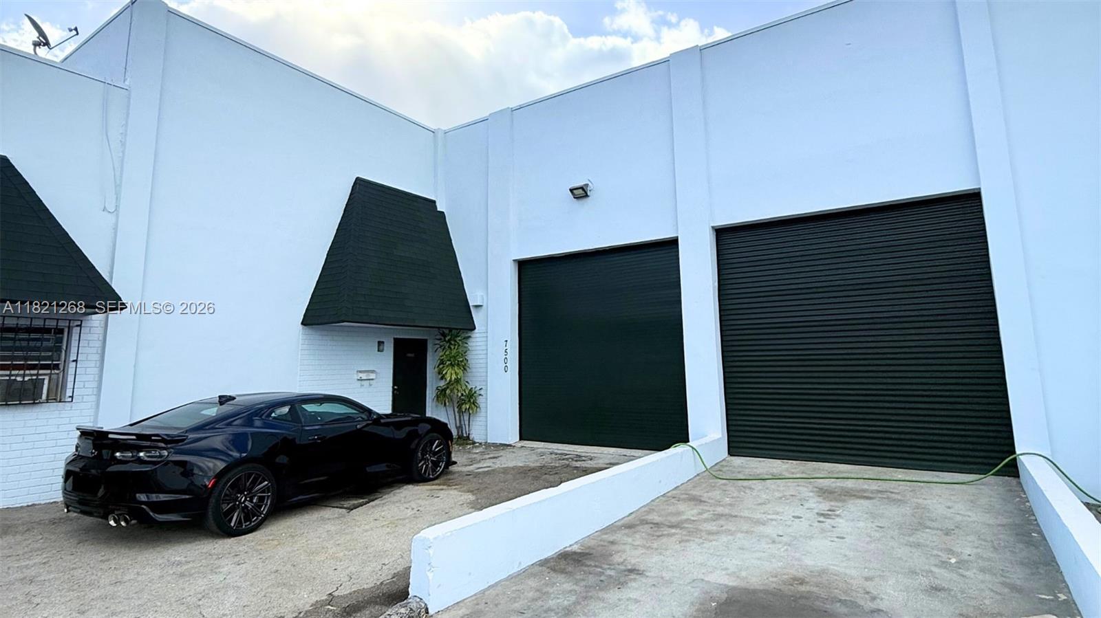 A black sports car is parked in front of a white warehouse with two roll-up doors — 7460 NW 82nd # 7500, Medley FL 33166, MEDLEY, FL