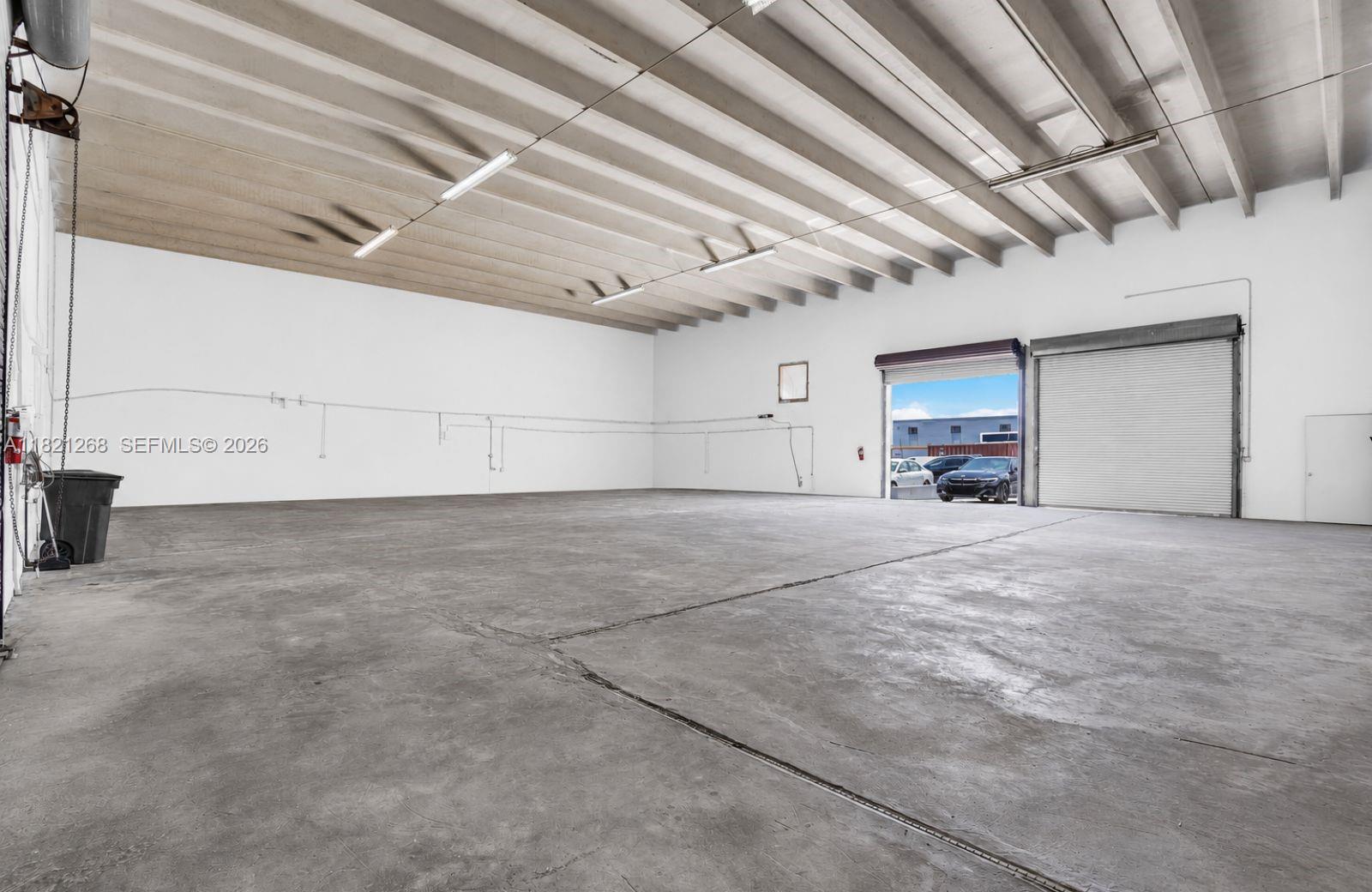 An empty industrial warehouse space features a concrete floor, white walls, and a roll-up door — 7460 NW 82nd # 7500, Medley FL 33166, MEDLEY, FL