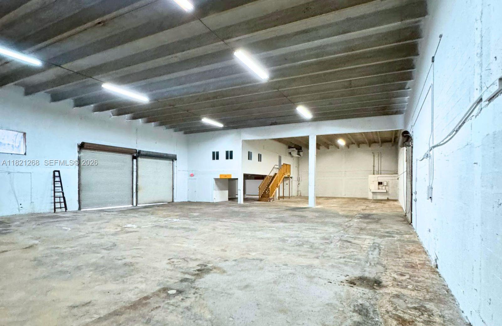 An empty industrial warehouse space features a concrete floor, high ceilings, and wooden stairs — 7460 NW 82nd # 7500, Medley FL 33166, MEDLEY, FL