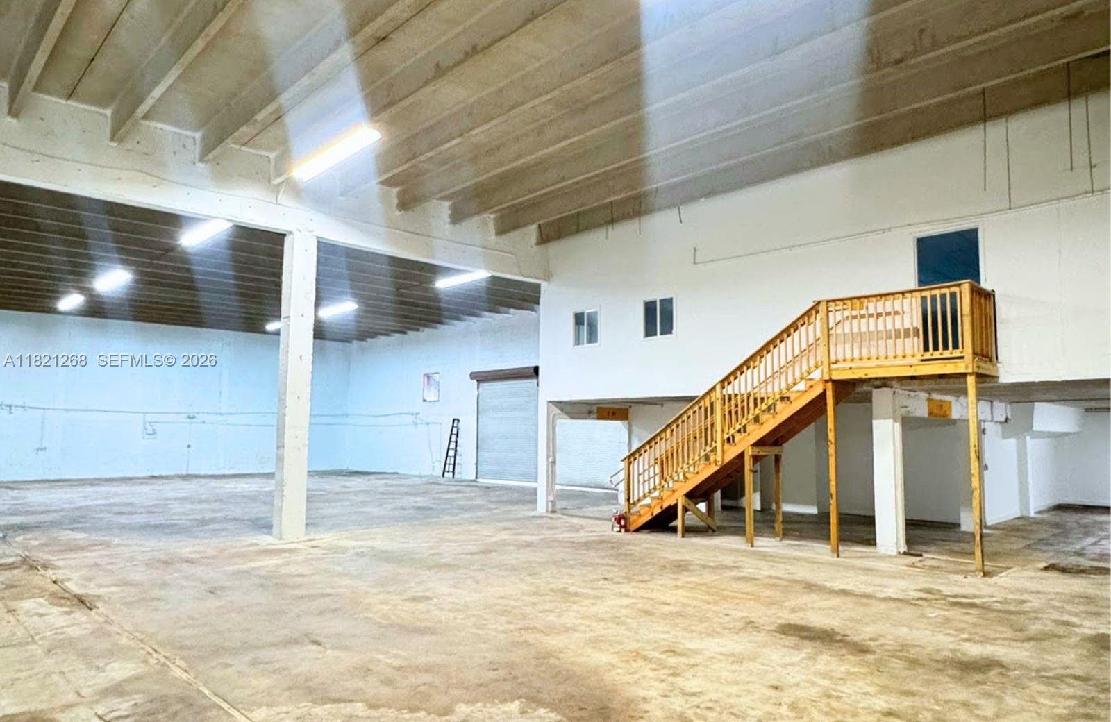 An industrial warehouse space features a concrete floor, exposed ceiling beams, and a wooden staircase — 7460 NW 82nd # 7500, Medley FL 33166, MEDLEY, FL