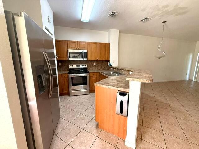 A kitchen features stainless steel appliances, wood cabinets, and a peninsula counter with tile flooring — 460 Princess Drive, Margate FL 33068, MARGATE, FL