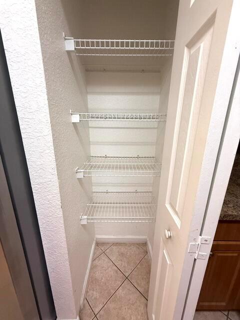 A narrow pantry closet features white wire shelving mounted on textured walls above tiled flooring — 460 Princess Drive, Margate FL 33068, MARGATE, FL