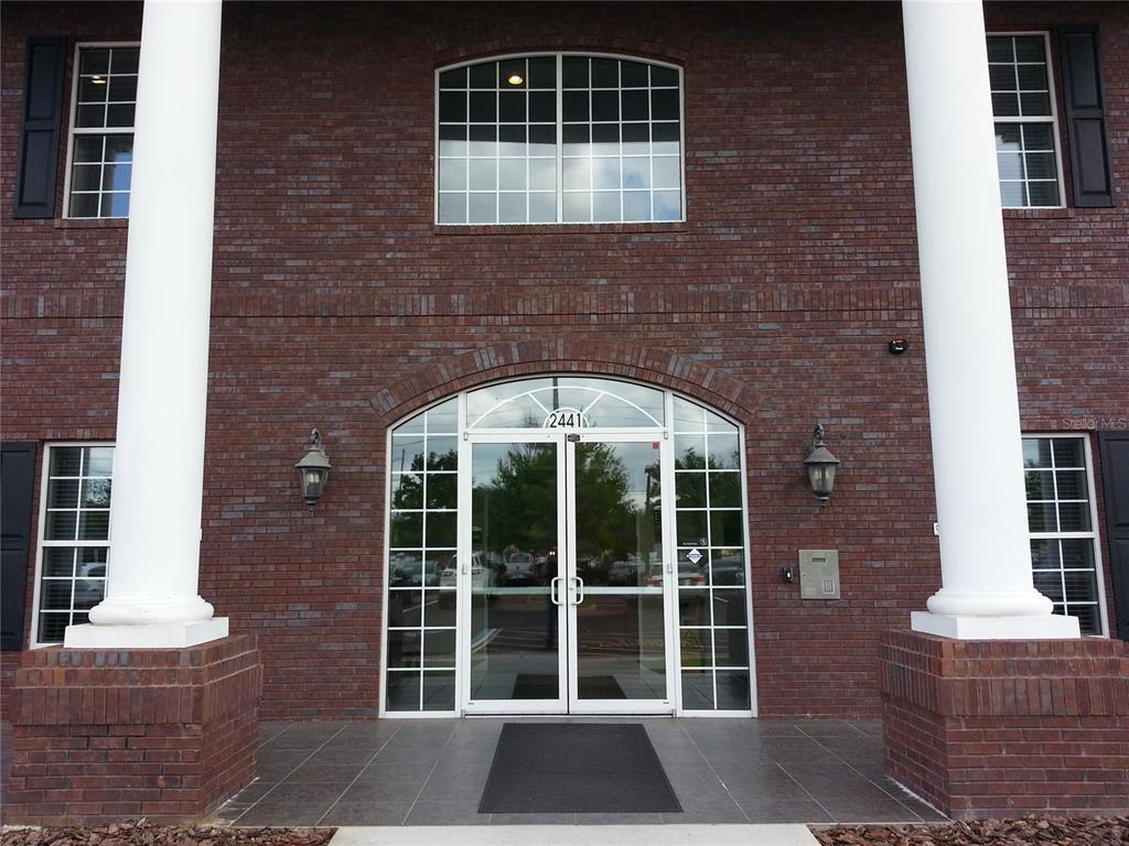 The exterior of a brick building features a glass double-door entrance with white columns — 2461 W STATE ROAD 426 UNIT 1021, OVIEDO, FL