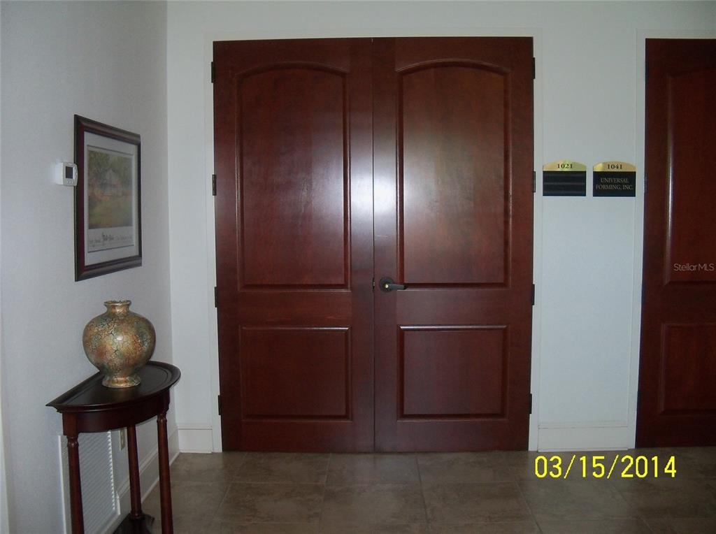 A wooden double door entrance features a small side table with a vase and artwork — 2461 W STATE ROAD 426 UNIT 1021, OVIEDO, FL
