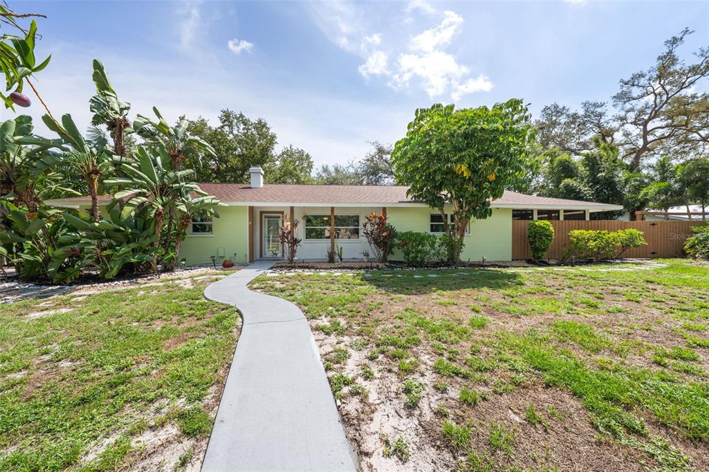 A single-story house with a light green exterior, a front walkway, and surrounding tropical landscaping — 7311 BROUGHTON STREET, SARASOTA, FL