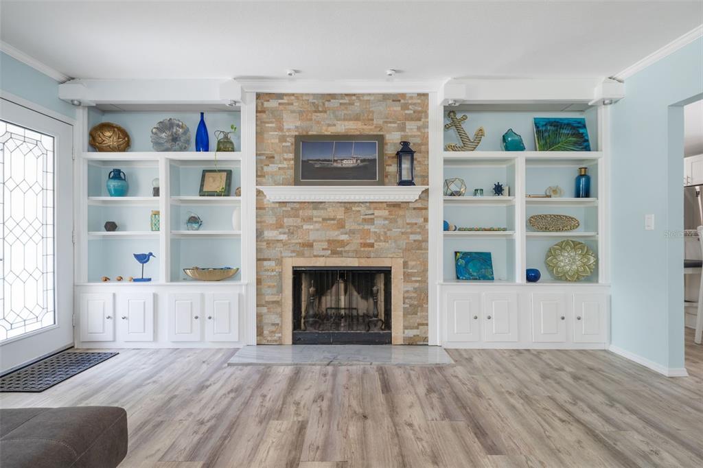 A living room features a stone fireplace flanked by white built-in shelves and wood flooring — 7311 BROUGHTON STREET, SARASOTA, FL