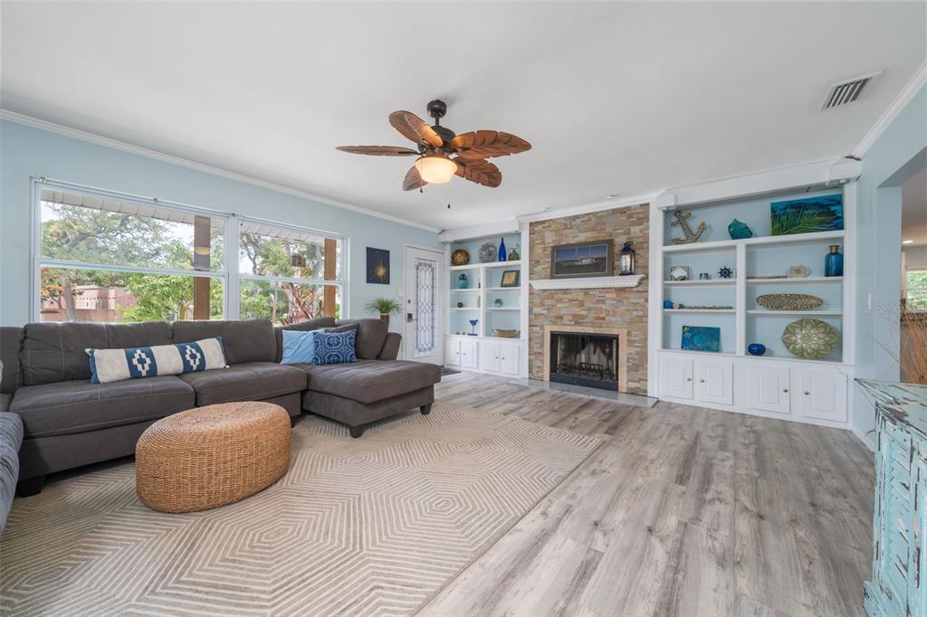 A living room features a stone fireplace, built-in shelving, a gray sectional, and wood-look flooring — 7311 BROUGHTON STREET, SARASOTA, FL