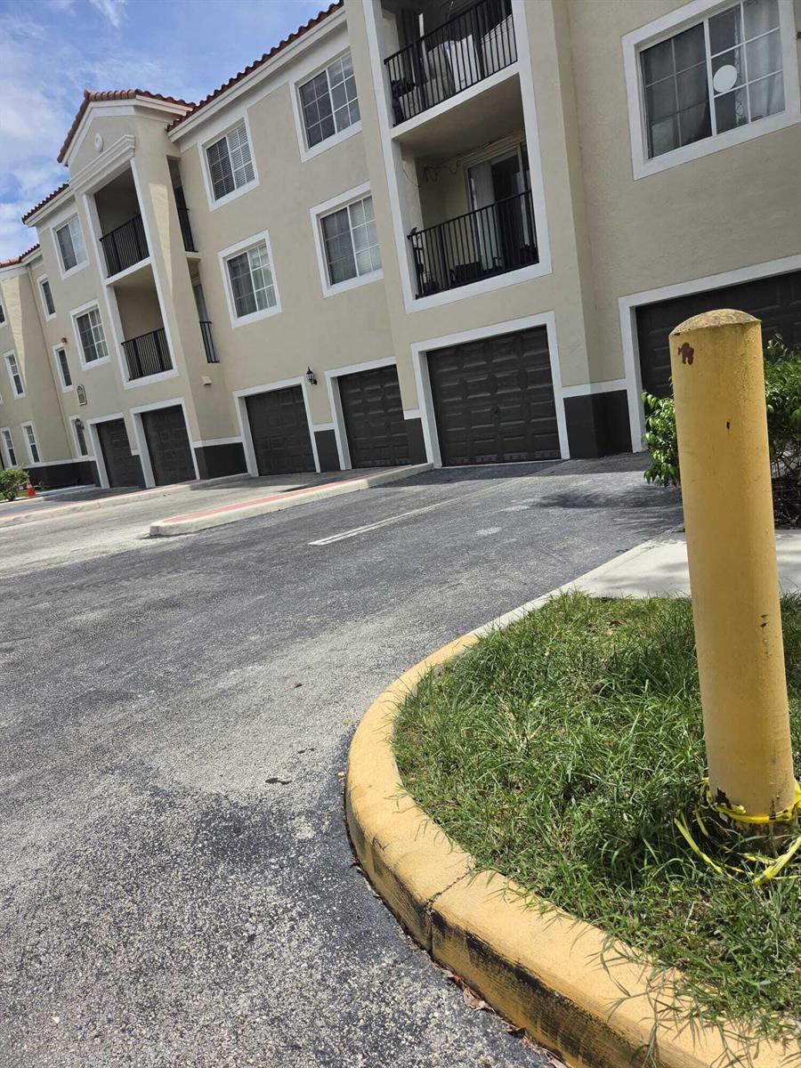An exterior view of a multi-story apartment building with attached garages and a yellow bollard — 2160 E Preserve Way # 201, Miramar FL 33025, MIRAMAR, FL