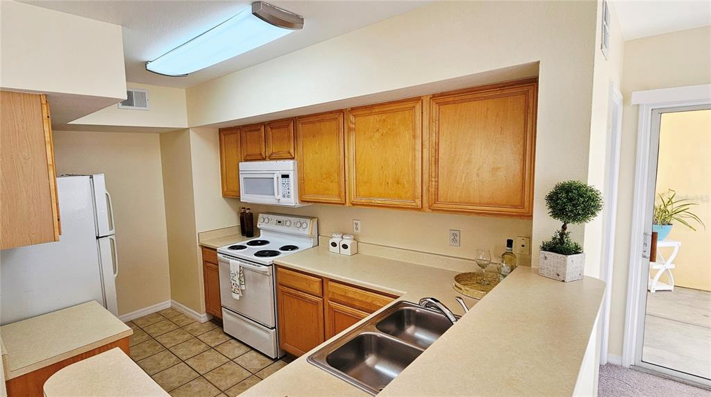 A kitchen features light wood cabinets, white appliances, a double sink, and tiled flooring — 1040 VILLAGIO CIRCLE UNIT 201, SARASOTA, FL