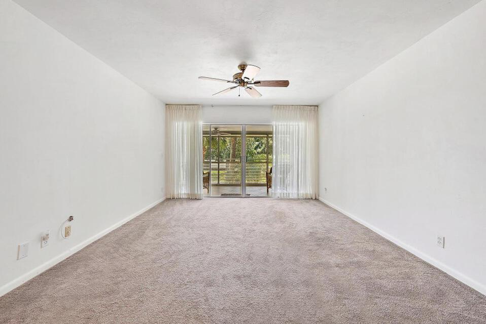 An empty living room with beige carpet, white walls, a ceiling fan, and sliding doors — 2 Garden Street # 203m, Tequesta FL 33469, TEQUESTA, FL