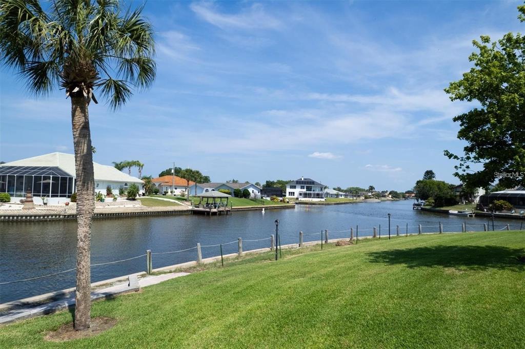A view of a canal from a grassy backyard with a palm tree — 44 CLUBHOUSE DRIVE UNIT 105, PALM COAST, FL